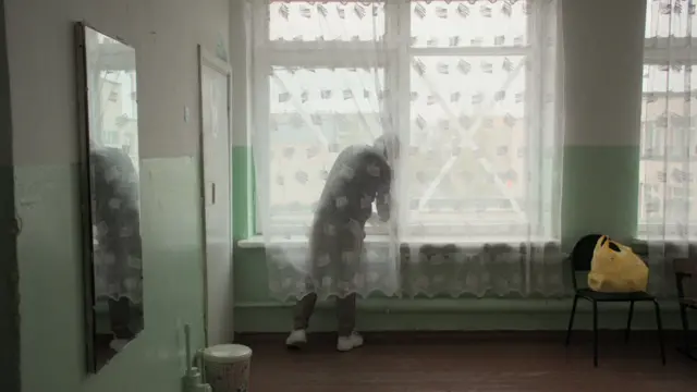 Pasha atrás de uma cortina colocando X em janelas 