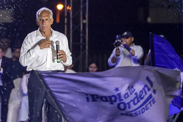 Nasry Asfura en un escenario durante la campaña electoral. Frente a él se ve una bandera en la que dice: "¡Papi a la orden! Presidente". 