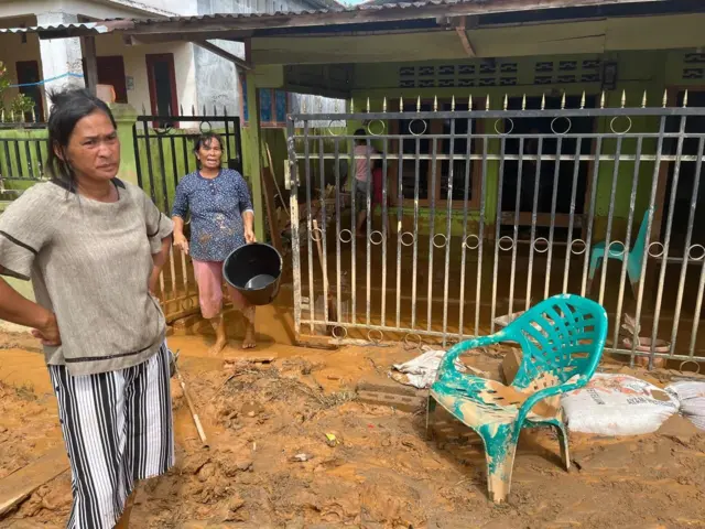 Dua perempuan sedang berjibaku membersihkan lumpur di depan rumahnya.