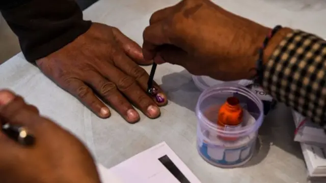 एक मतदाता के हाथ में स्याही लगाता चुनाव कर्मचारी