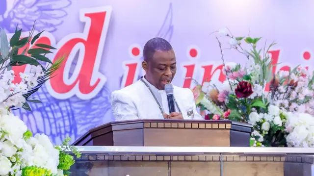 Pastor Daniel Olukoya wear all-white for di Cross-Over service for 2024 as e stand for pulpit wit microphone.