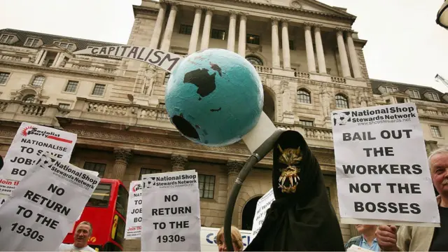 13 Ekim 2008'de Londra'da İngiltere Merkez Bankası önünde düzenlenen bir protesto sırasında, bir ölüm meleği figürü, tırpanla delinmiş bir dünya küresi tutuyor.
