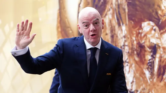 Przewodniczący FIFA Gianni Infantino przemawia, trzymając prawą rękę w górze. Jest ubrany w granatowy garnitur i krawat.