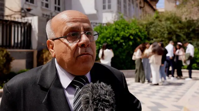 صورة لرجل يرتدي بدلة رسمية ويتحدث للمايكروفون.