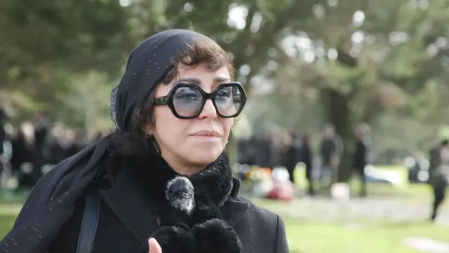 تصویری از شبنم طلوعی در لباس سیاه. پشت سرش مزار بهرام بیضایی دیده میشود.