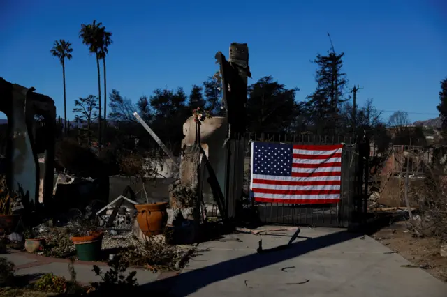 پرچم آمریکا که بر دروازه حیاط خانه‌ای که کاملا سوخته آویزان شده ادست