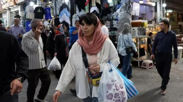 Mujer lleva una bolsa con motivos violeta en medio de un mercado donde se destaca una tienda con