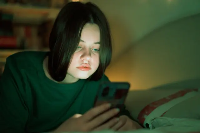 Jovem olha o telefone celular deitada, à noite