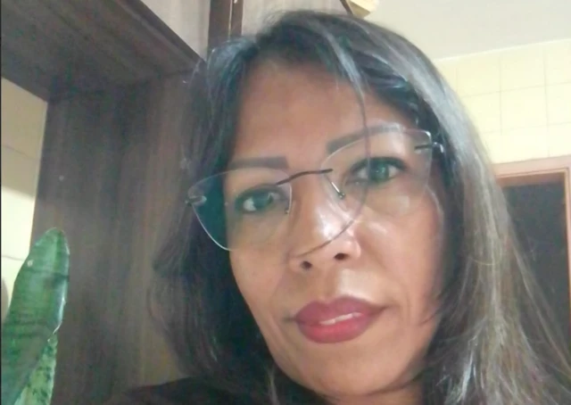 Damarys Lara, 49, usa óculos em uma selfie com uma planta ao fundo