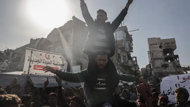 Wani mutum zaune kan kafaɗar wani mutimin a cikin ɗaruruwan maza riƙe da alluna a Beit Lahiya