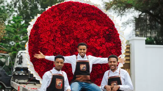 ተሽከርካሪ ላይ የተጫነ ግዙፍ የአበባ እቅፍ ፊት ለፊት የሚታዩ ሠራተኞች
