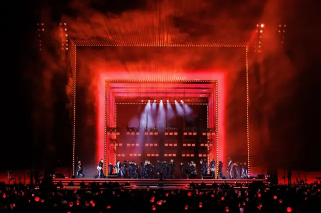 A wide shot of the stage turned red with dancers on stage and fans in the crowd