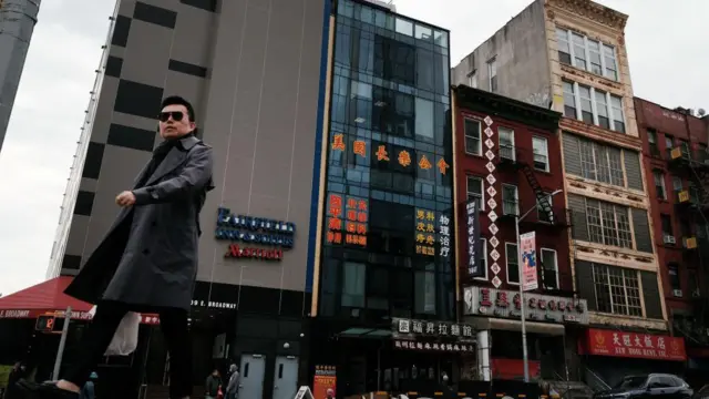 Siyah trençkotlu bir adam, Manhattan'ın Çin Mahallesi'nde bir dizi binanın önünde yürüyor