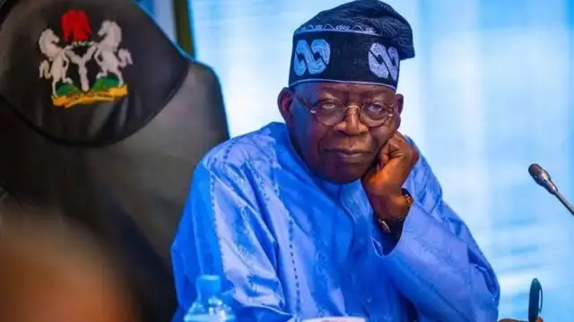 Bola Tinubu zaune a ofishinsa ya yi tagumi, sanye da gilashi
