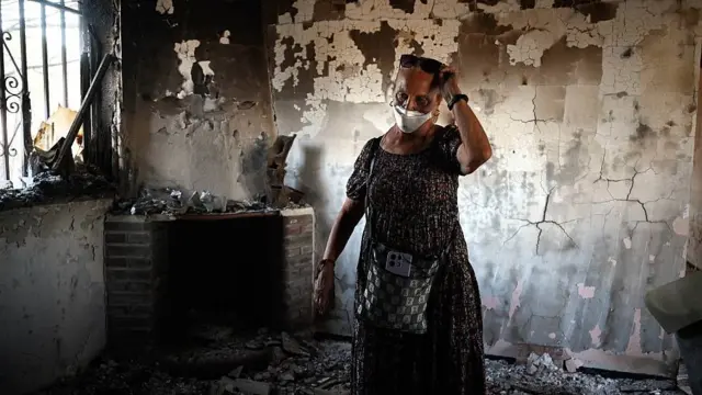 Concepción García parada en medio de una habitación destruida por el fuego en la que se ve el techo y las paredes ennegrecidas y calcinadas