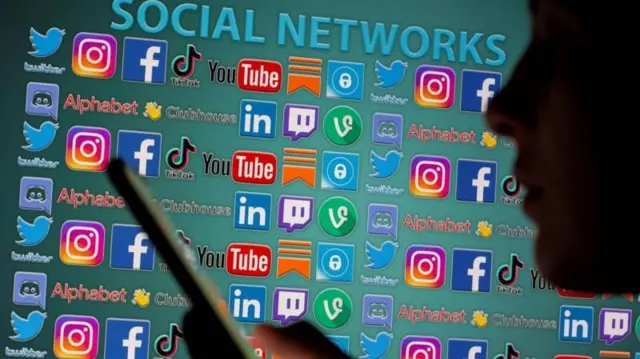 विभिन्न सामाजिक सञ्जालका लोगोको पृष्ठभूमिमा फोन चलाउँदै एक व्यक्ति