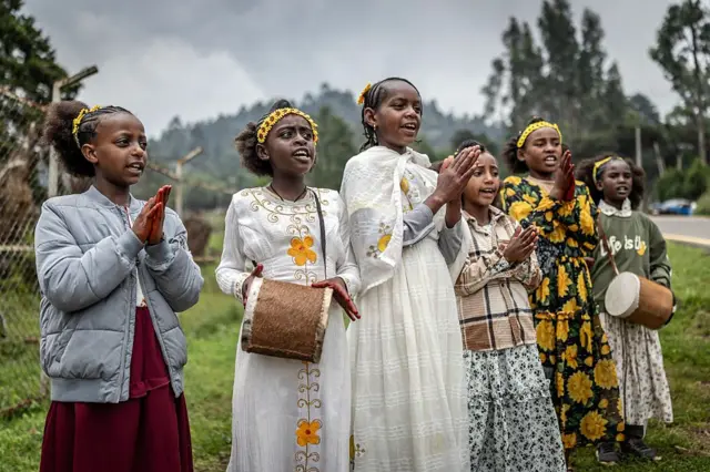 مجموعة من الفتيات يرتدين زهورًا صفراء، رمز السنة الجديدة، يعزفن على الطبول ويغنين أغانٍ موسمية على جانب الطريق للمارّة، كجزء من تقاليد رأس السنة الإثيوبية في أديس أبابا.