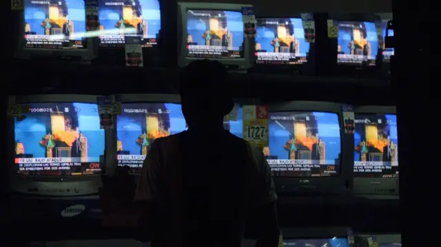 مشاة غواتيماليون يشاهدون على شاشة التلفزيون في مدينة غواتيمالا، في 11 سبتمبر 2001 ، لحظة اصطدام طائرة ثانية، استولى عليها مختطفون مجهولون، بمركز التجارة العالمي في نيويورك.