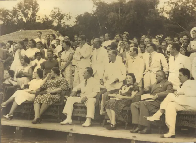 Foto antiga com público de homens e mulheres sentados e em pé 