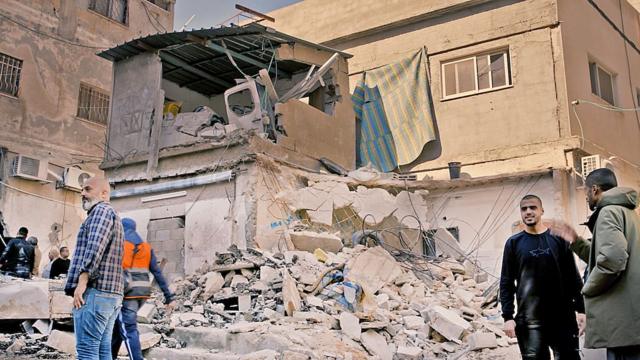 Homens palestinos em meio aos escombros de um prédio de concreto
