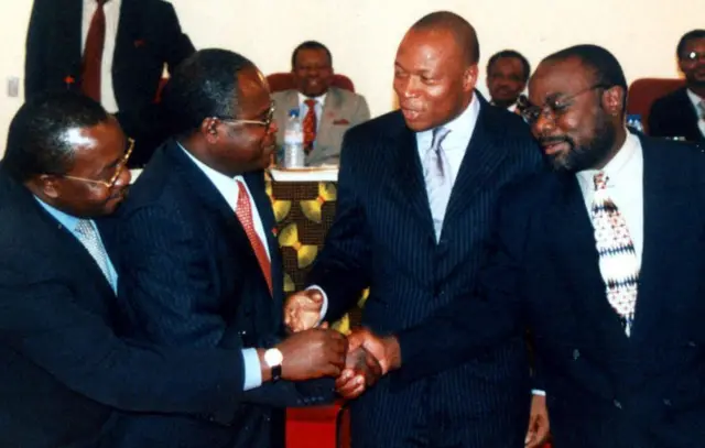 I Lusaka muri Zambia muri Gicurasi(5) 2001 mu biganiro hagati y’Abanyecongo ubwabo, ku ifoto hariho John Tibasima (ubanza ibumoso) wari uhagarariye umutwe wa RCD-Goma, Joseph Muduimbi (wa kabiri ibumoso) wari uhagarariye RCD-Kisangani, Minisitiri Kongolo Jeannot Mwenze wari Minisitiri w’umutekano wa RDC, na Dominique Kanku wari uhagarariye umutwe wa MLC ubwo bahanaga ibiganza nyuma yo kugera ku kumvikana