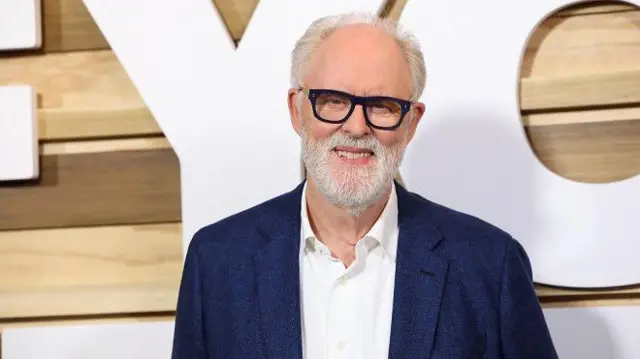 John Lithgow sorrindo em frente a painel de evento