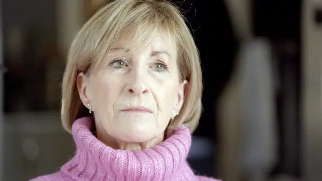 Alison Cocks, mulher loira de meia idade, veste suéter rosa 