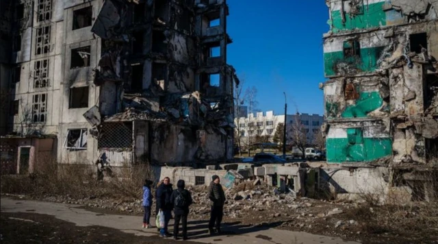 Quatre personnes sont devant un immeuble à moitié démoli