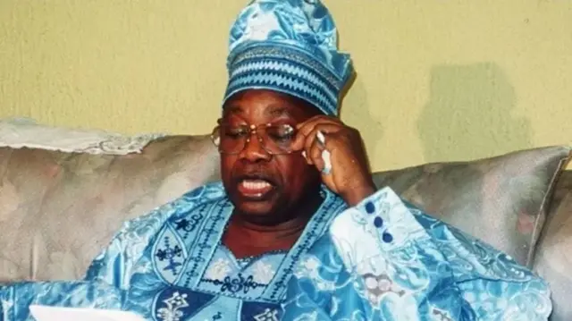 MKO Abiola dey read from paper as hold im eyeglass