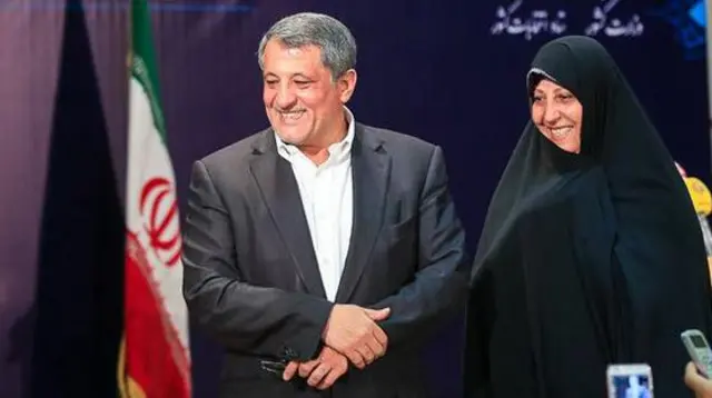 فاطمه هاشمی در کنار محسن هاشمی، پرچم جمهوری اسلامی ایران در پس زمینه