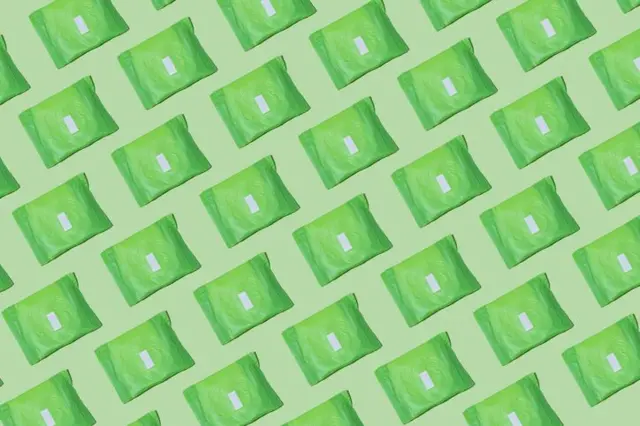 Yeşil plastik görünümlü ambalaja sarılı hijyenik pedler çaprazlama yanyana dizilmiş yeşil bir arka planda duruyor 