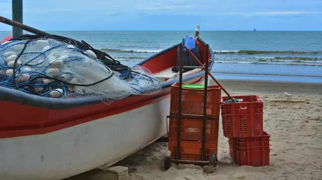Barco na areia com rede de pesca e alguns caixotes para peixes