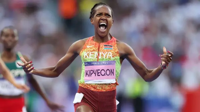 Faith Kipyegon showing her emotion wit her mouth open and hand wide apart