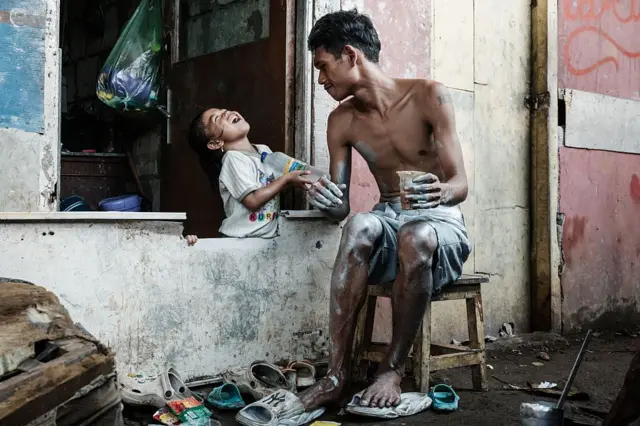 Pengamen jalanan Keris Munandar bercanda dengan putrinya, sebelum mengecat tubuhnya dengan perak di depan rumahnya di Jakarta. Dia bekerja sebagai "manusia silver".