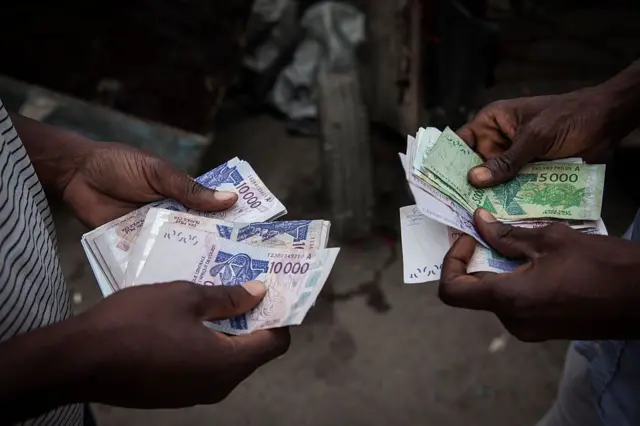Deux hommes comptent les billets de francs CFA d'Afrique de l'Ouest pour les échanger sur le marché noir à Abidjan, en Côte d'Ivoire