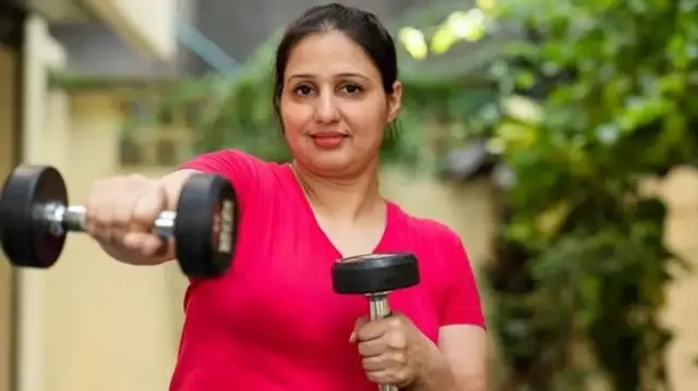 ඩම්බෙල් දෙකක් ආධාරයෙන් ව්‍යායම කරන කාන්තාවක්‌ 