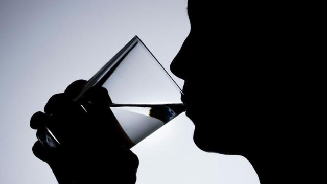 Pessoa, em foto tirada contra a luz, bebe água em copo