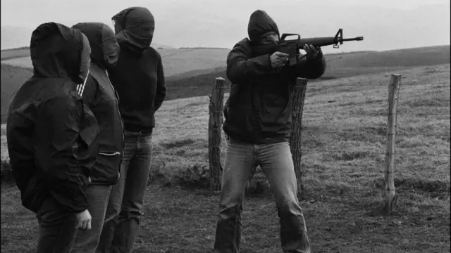 Membro encapuzado do ETA aponta um fuzil durante treinamento. Outros três militantes, também encapuzados, o observam em imagem de 1978.