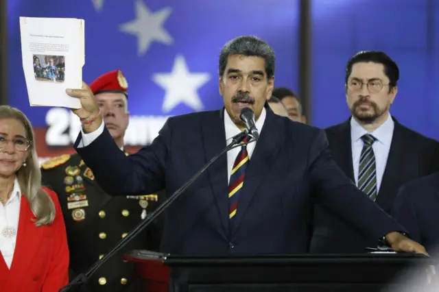 Nicolás Maduro discursando no microfone, rodeado por outras pessoas 