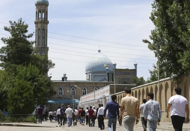 Men in t-shirts or shirts and trousers arrive to pray at a mosque in Dushanbe, Tajikistan, 2019