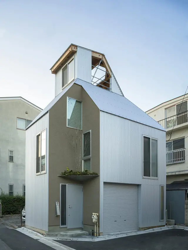 Casa urbana de diseño contemporáneo con techo inclinado, revestimiento metálico blanco y pequeña terraza en la parte superior.