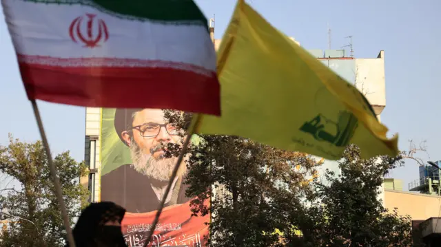 صورة تظهر العلم الإيراني إلى جانب راية حزب الله ومن خلفهما تبدو صورة القيادي الراحل في الحزب هاشم صفي الدين.