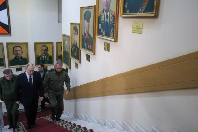 Герасимов, Путин и Шойгу поднимаются по ступенькам. На стенах портреты военачальников
