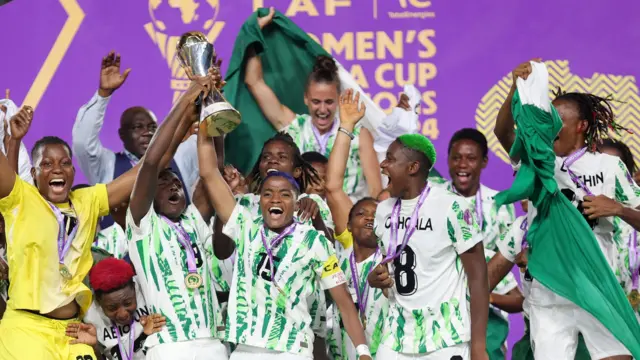 Les joueuses nigérianes célèbrent leur victoire avec le trophée de la Coupe d'Afrique des Nations Féminine 2024, leur capitaine Rasheedat Ajibade au premier plan, le brandissant au-dessus de sa tête de la main droite.