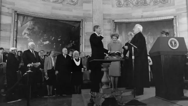 Ronald Reagan holds his hand on a bible and takes the oath of office as people look on in the Capitol Rotunda.