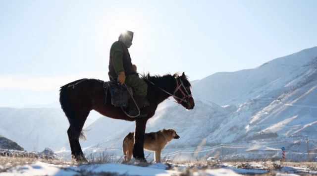 Man on a horse, with dog next to him on the snowy mountains of Kyrgyzstan