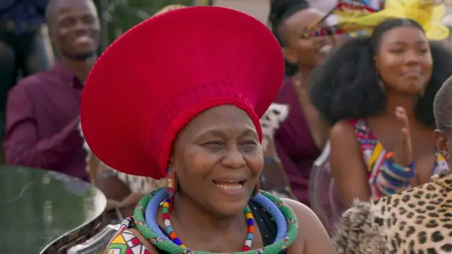 Nandi Nyembe akina muri film aho yambaye inkofero kavukire itukura n'ibitsibo vy'ubudede. 