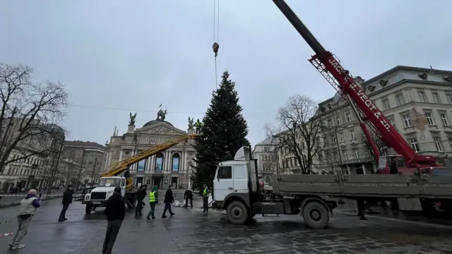 Кран ставить ялинку біля оперного театру у Львові, робочі ходять біля машини
