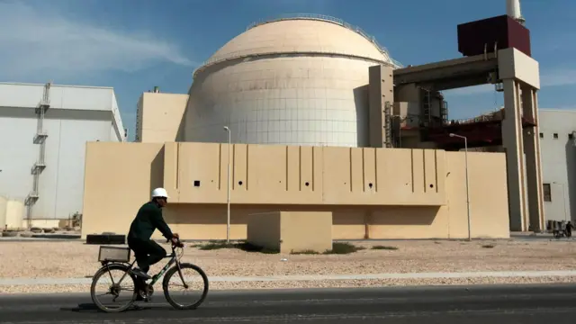 Un ouvrier portant un casque blanc roule à vélo devant le bâtiment du réacteur de la centrale nucléaire de Bushehr, juste à l'extérieur de la ville méridionale de Bushehr, en Iran, en octobre 2010.