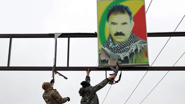 Suriye askerleri, Rakka'nın Tabka ilçesinde asılı Abdullah Öcalan posterini indiriyor. Askerler resmi indirmek için ellerindeki tüfeklerini kullanıyor. 